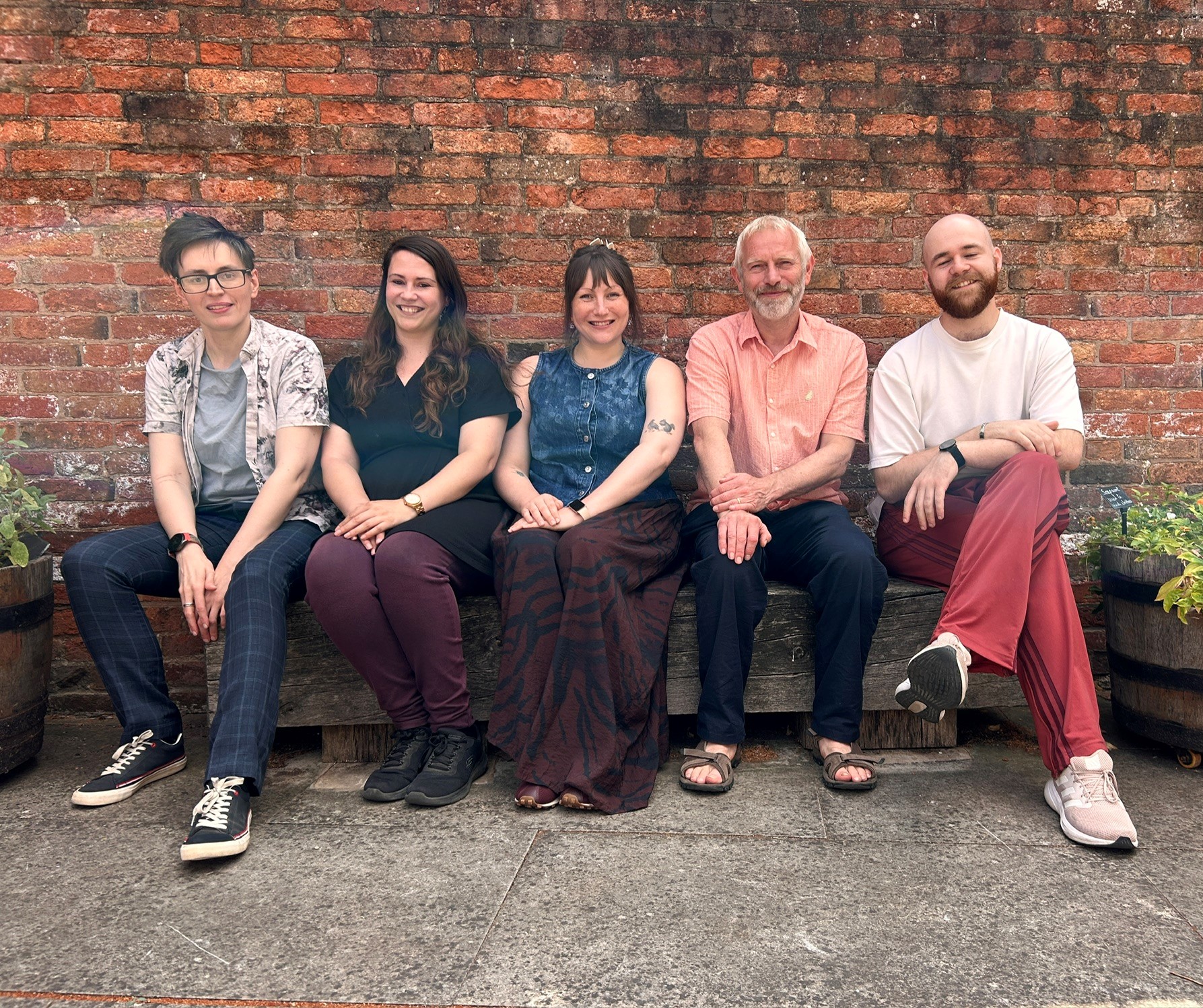 Five people sitting on a bench in front of a brick wall and smiling