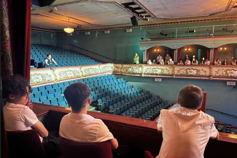 Three school children watching a performance from box seats in a theatre