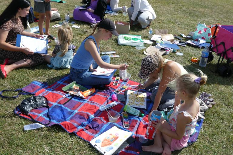 An open air arts session enjoyed by many families on picnic blankets