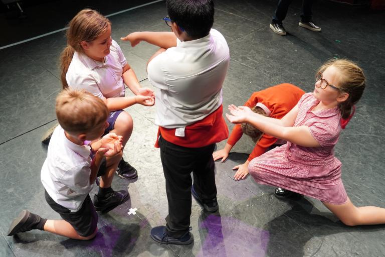 Four children in school uniforms performing a dramatic scene on a dark stage.